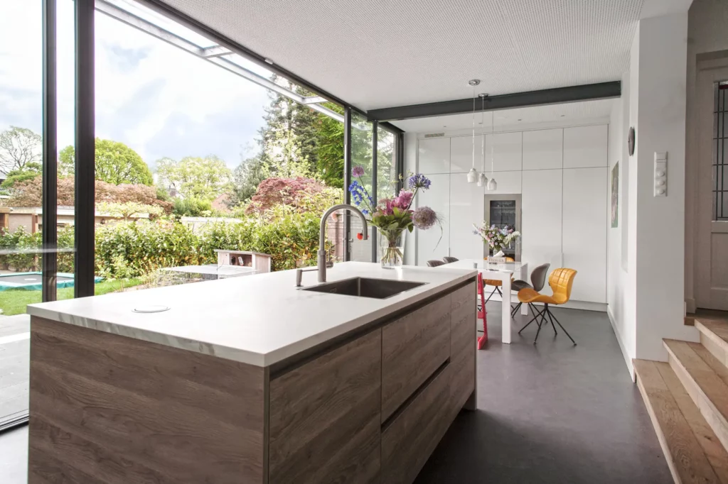 Moderne industriele keuken aluminium schuifpui opent naar de tuin spoeleiland met wit marmeren blad